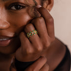 Model wearing a gold checkered band ring featuring alternating rows of emerald and diamond round-cut CZ stones set in an openwork grid design.