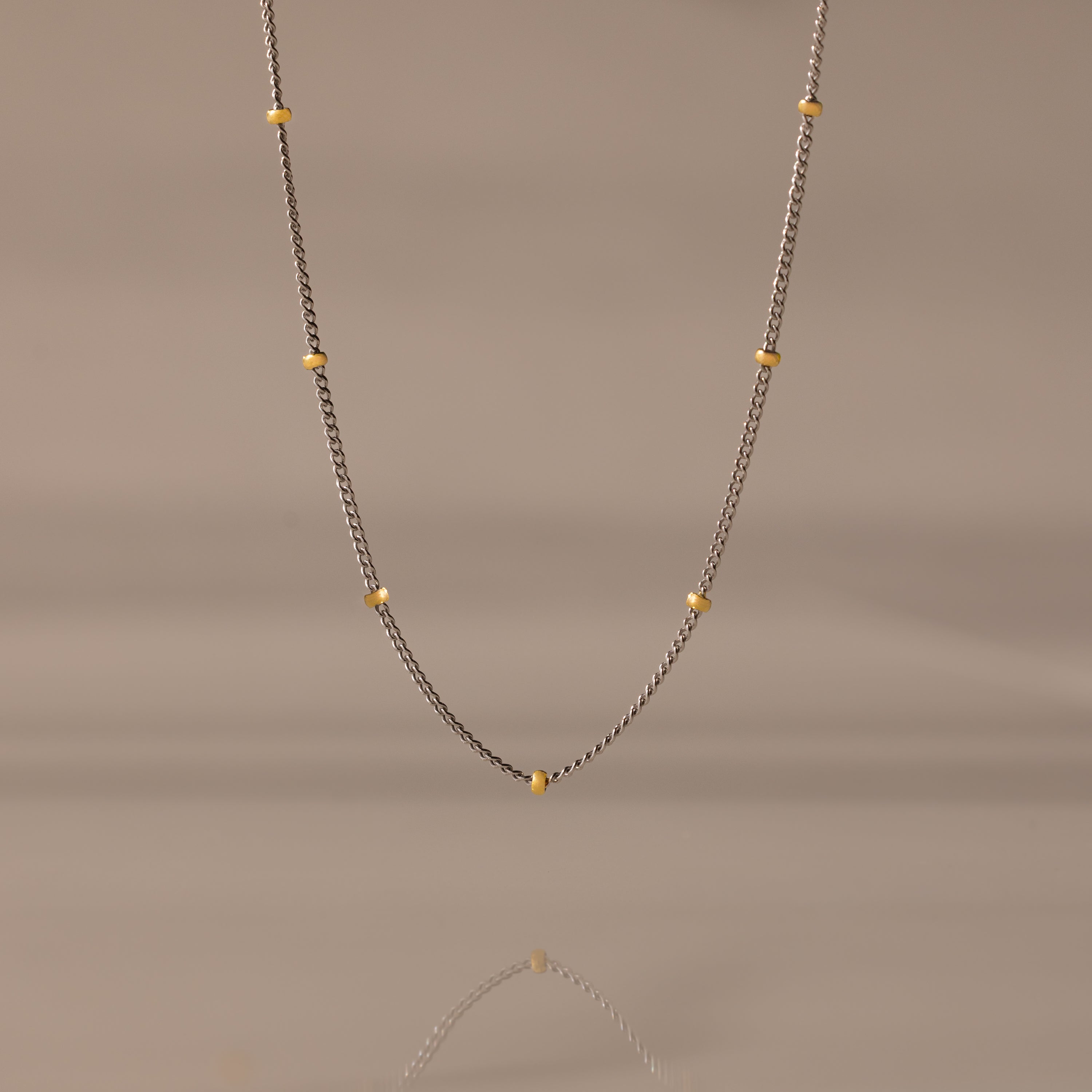 The Mixed Metal Beaded Necklace features a silver satellite chain with small gold beads evenly spaced—ideal for layering.