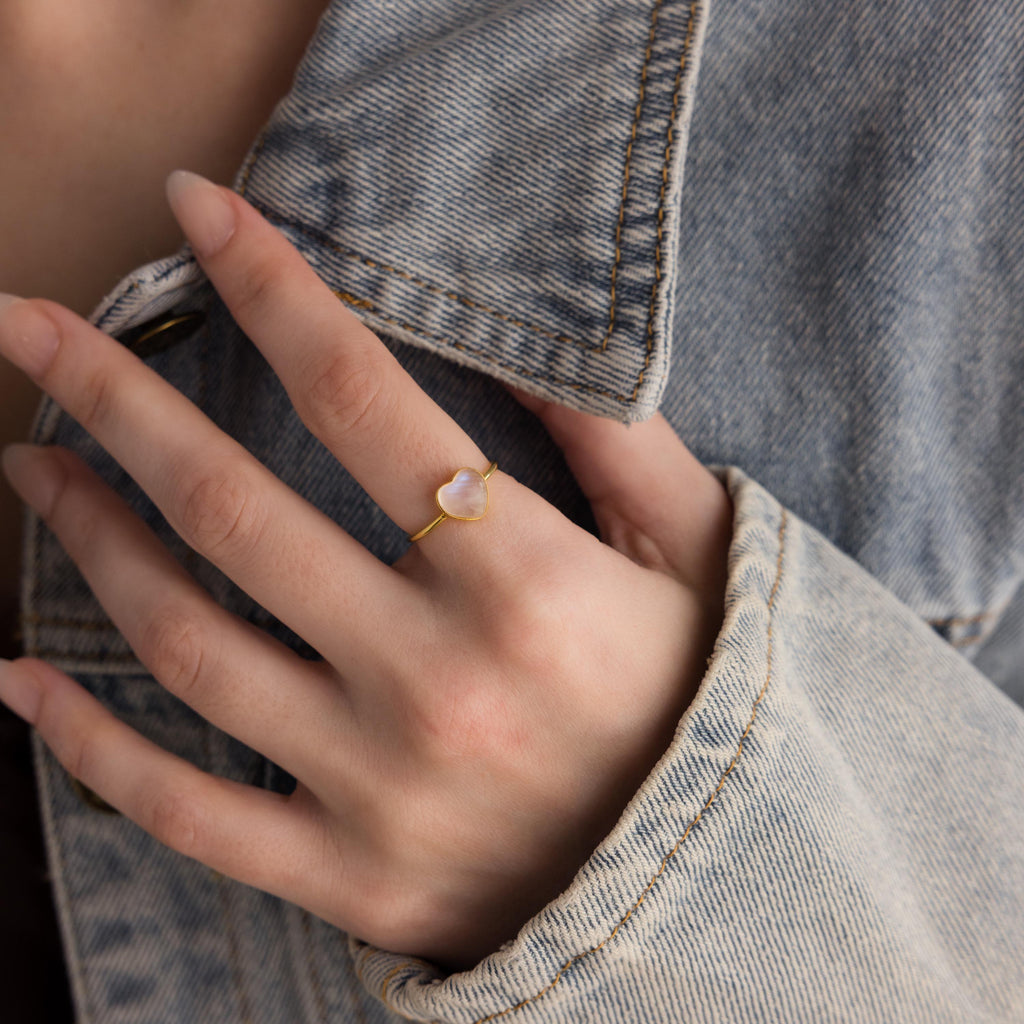 A hand adorned with the Moonstone Heart Ring shines atop a denim jacket sleeve.