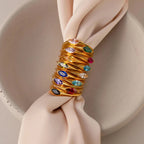 The Marquise Birthstone Signet Ring, featuring a marquise-cut gemstone, is stacked with gold rings and wraps around a pale pink fabric napkin in a ceramic bowl.