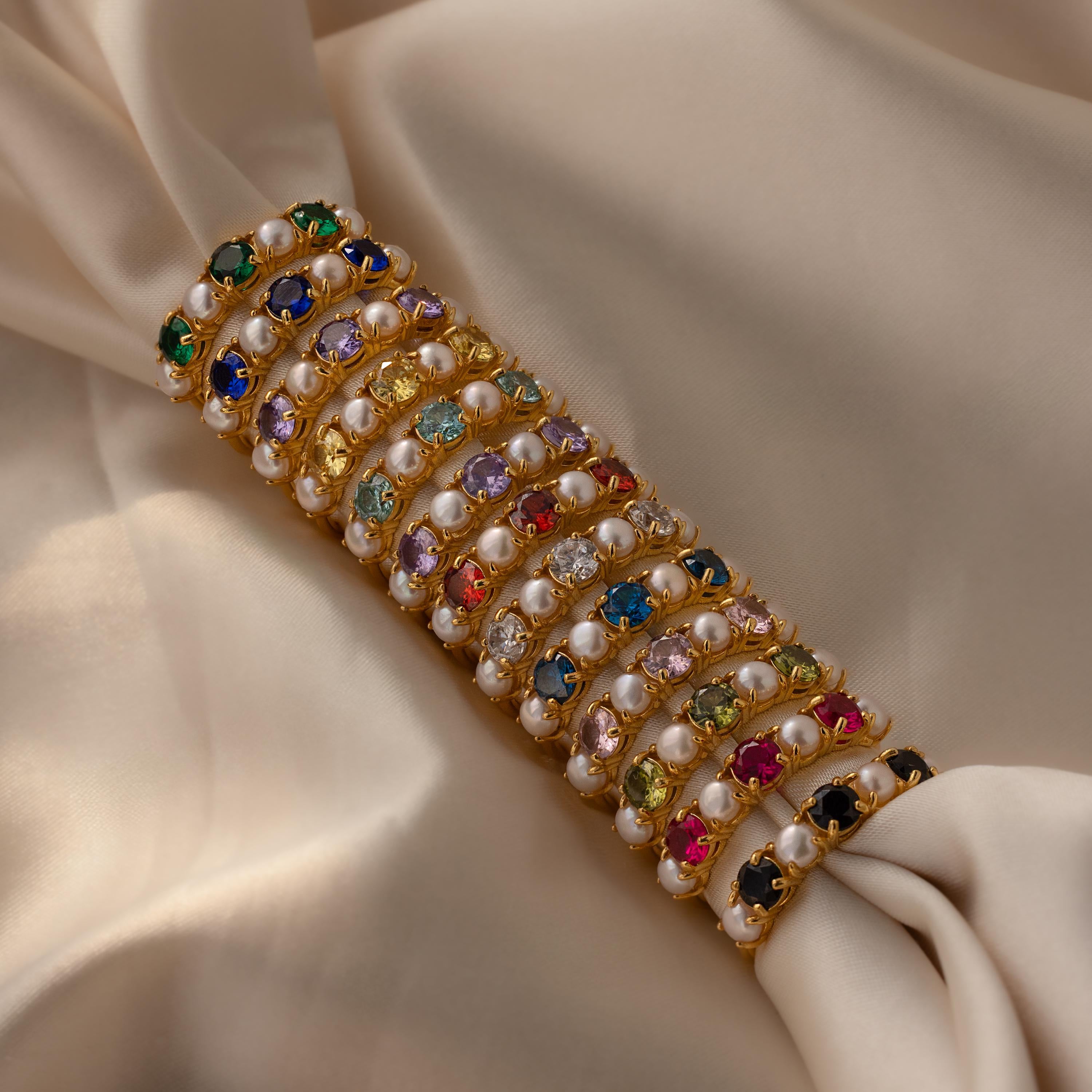 The Birthstone Pearl Lace Ring, adorned with lustrous pearls and striking gemstones, is displayed on light beige satin fabric.