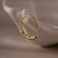 The Beaded Multiple Name Ring, featuring three engraved beads, is displayed on a white, curved ceramic surface.