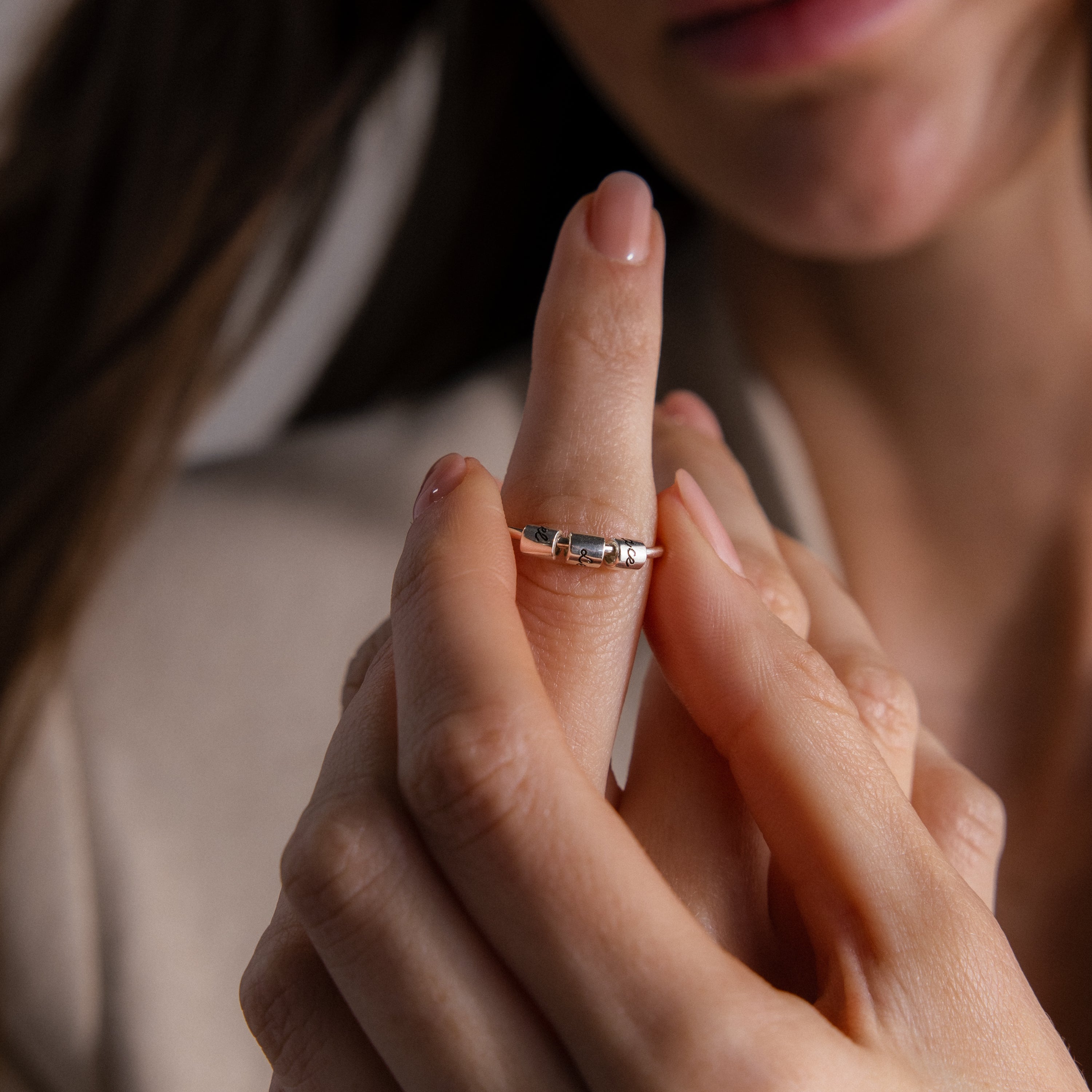 A woman’s hand slides the Beaded Multiple Name Ring in Sterling Silver onto her finger, close-up view.