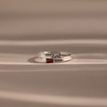Two Toi et Moi Baguette Name Rings in Sterling Silver, each with colored gemstones and engraved names, Chloe and Sarah, rest on a soft beige surface—a perfect personalized gift for two.