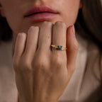 A close-up of a hand wearing two gold rings with blue stones, including the chic Toi et Moi Baguette Name Ring in Rose Gold, held near a person’s face.