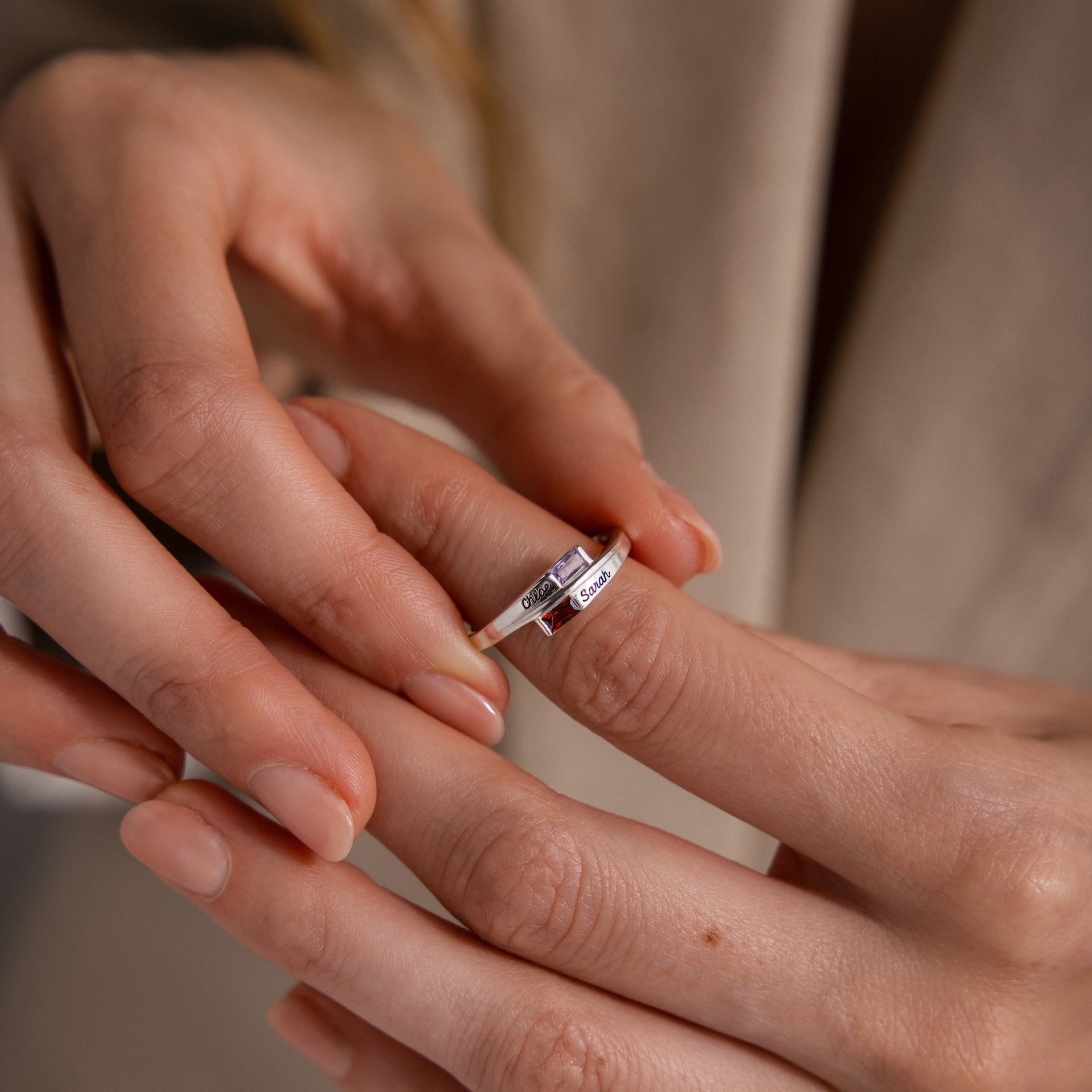 A hand wearing a silver Toi et Moi Baguette Name Ring with personalized engraving gently touches another finger, capturing a moment of connection.