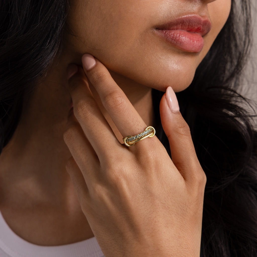 A woman touches her chin, wearing the Duo Blue Zircon Tennis Linked Ring Set with a twisted design on her finger.