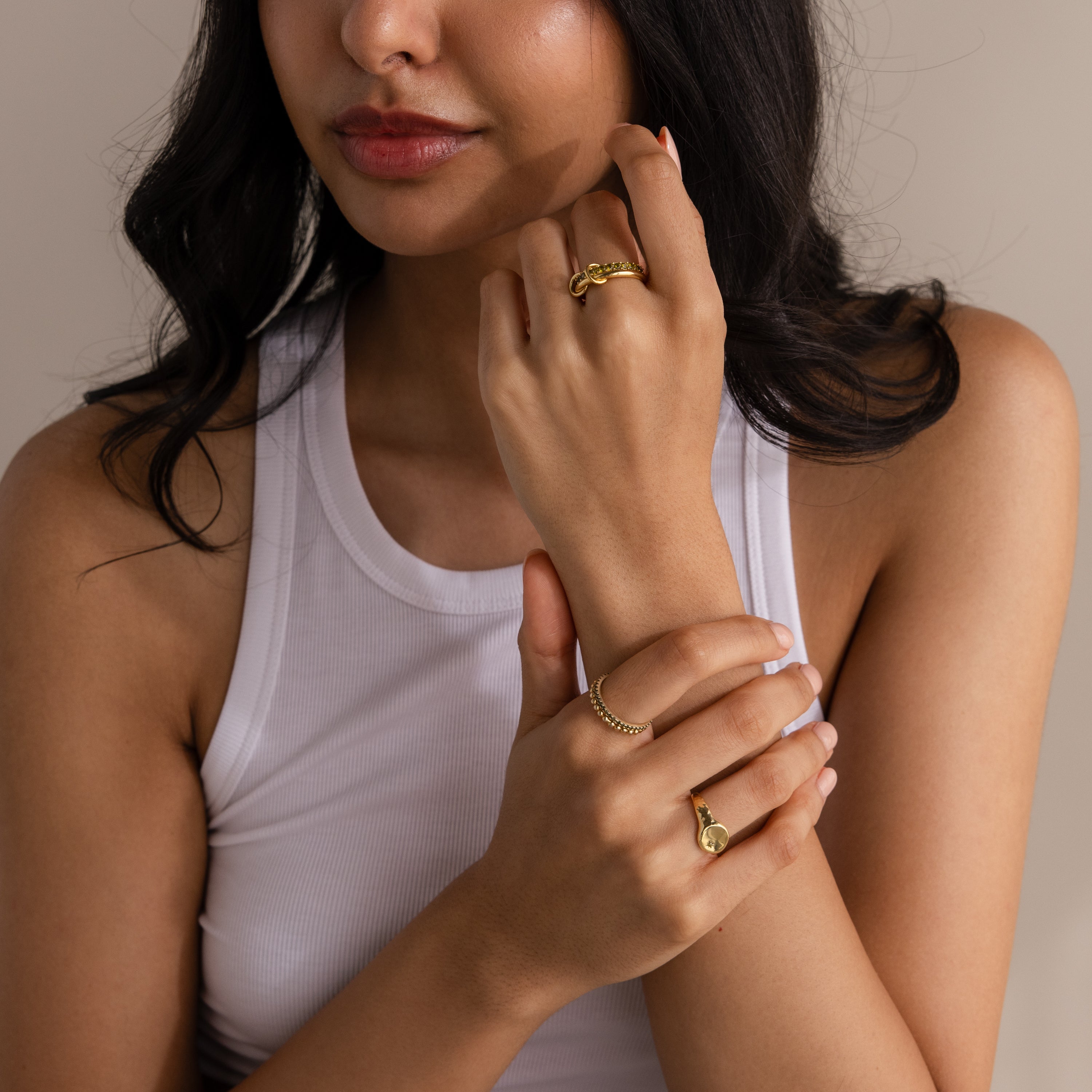 Woman in a white tank top wears the Duo Ruby Tennis Linked Ring Set and several gold rings, hands raised near her face.
