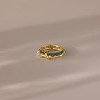 The Duo Birthstone Tennis Linked Ring Set in Blue Zircon (December) features blue gemstones set in a row on gold, displayed on a neutral, softly lit surface.
