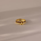 The Duo Birthstone Tennis Linked Ring Set in Garnet (January) features a minimalist, looped design with red gemstones, displayed on a soft neutral surface.