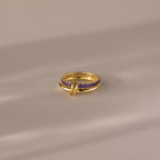 The Duo Birthstone Tennis Linked Ring Set in Amethyst (February) features minimalist gold loops and small purple stones, displayed on a smooth beige surface.