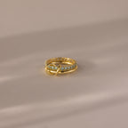 The Duo Birthstone Tennis Linked Ring Set in Aquamarine (March) features a minimalist gold band with blue stones, artfully displayed on a soft beige surface.