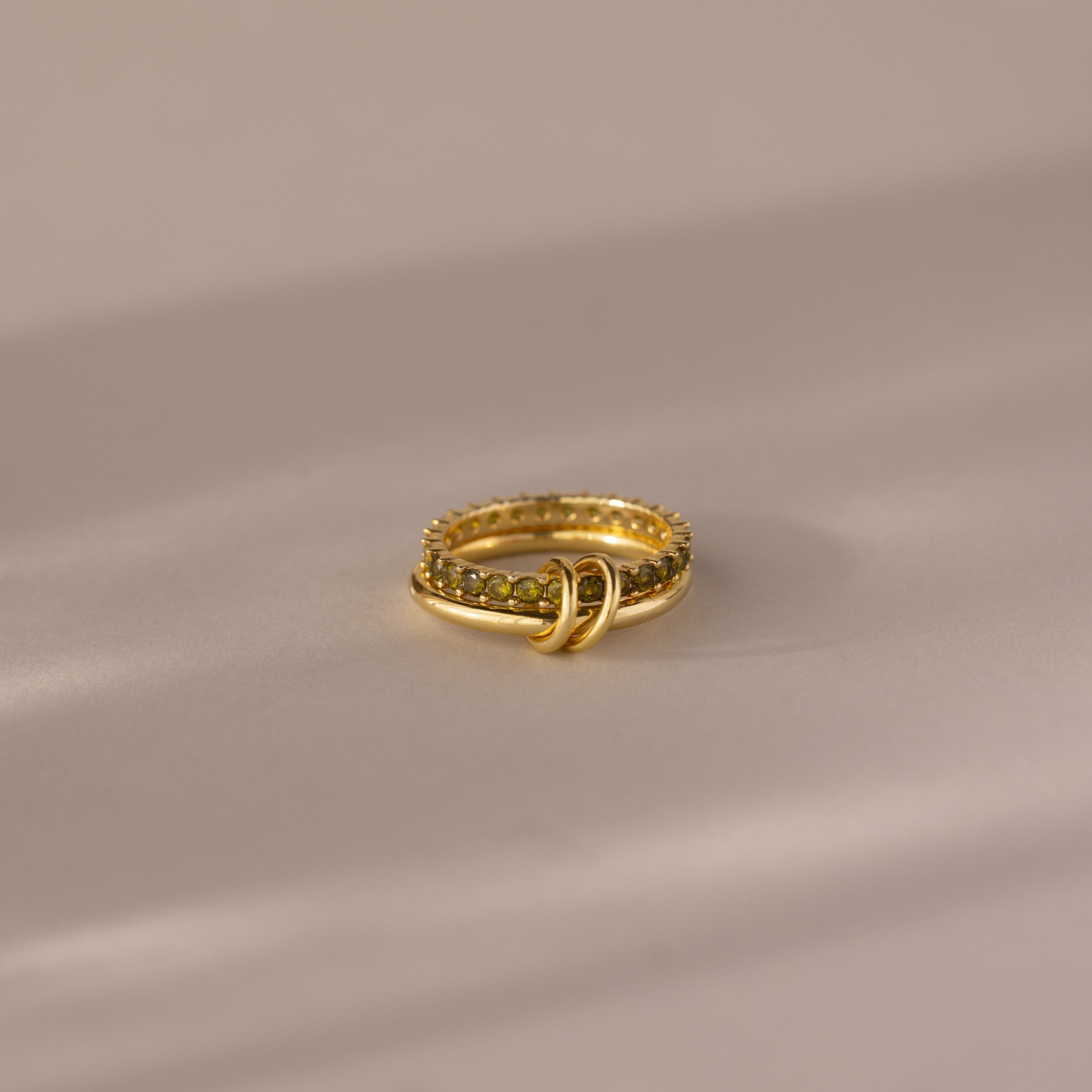 Duo Birthstone Tennis Linked Ring Set in Peridot (August), featuring a textured gold band with embedded stones, displayed on a soft, neutral surface.
