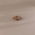 The Duo Blue Zircon Tennis Linked Ring Set features shimmering blue zircon stones in a row, showcased on a neutral beige surface.