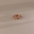 The Duo Pink Tourmaline Tennis Linked Ring Set, featuring rose gold bands and delicate pink stones, rests elegantly on a beige surface.