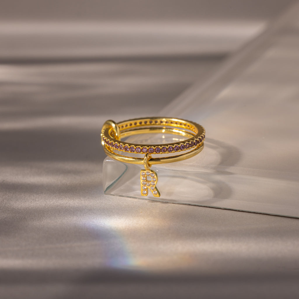 Linked Initial Birthstone Ring Set in Alexandrite (June), featuring a small dangling R charm with petite gemstones, displayed on a clear surface.