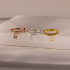 The Linked Initial Birthstone Ring Set features three rings—rose gold, silver, and gold—each with a dangling letter charm. Wear them stacked or solo for a personalized touch that adds unique style to any look.