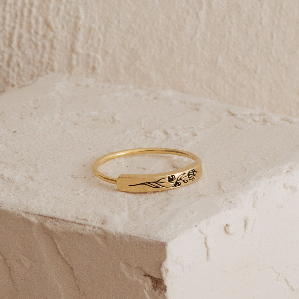 Gold ring with a floral design on a beige stone surface