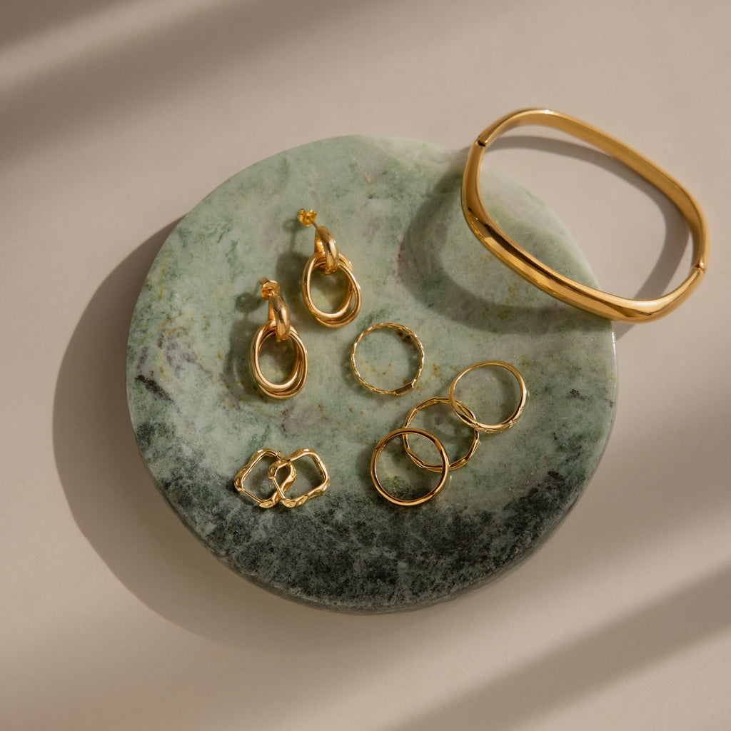 Gold earrings, rings, and a bracelet rest on the Marble Jewelry Dish, crafted from green marble and displayed on a beige surface.