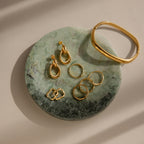 Gold earrings, rings, and a bracelet rest on the Marble Jewelry Dish, crafted from green marble and displayed on a beige surface.