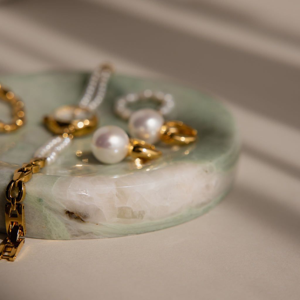 Gold jewelry and pearl earrings displayed on a round Green Marble Jewelry Dish with soft shadows.