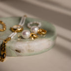 Gold jewelry and pearl earrings displayed on a round Green Marble Jewelry Dish with soft shadows.