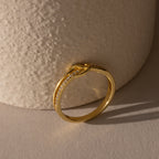 The Pave Knot Ring, featuring small embedded diamonds and a striking knot design, rests on a textured beige surface—an ideal jewelry gift.