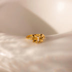 The gold Bow Pearl Ring is displayed on a softly lit, curved cream surface, highlighting its delicate design.
