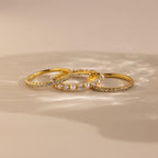 The Diamond Eternity Ring Set, featuring three gold rings, is displayed on a beige surface with soft lighting.