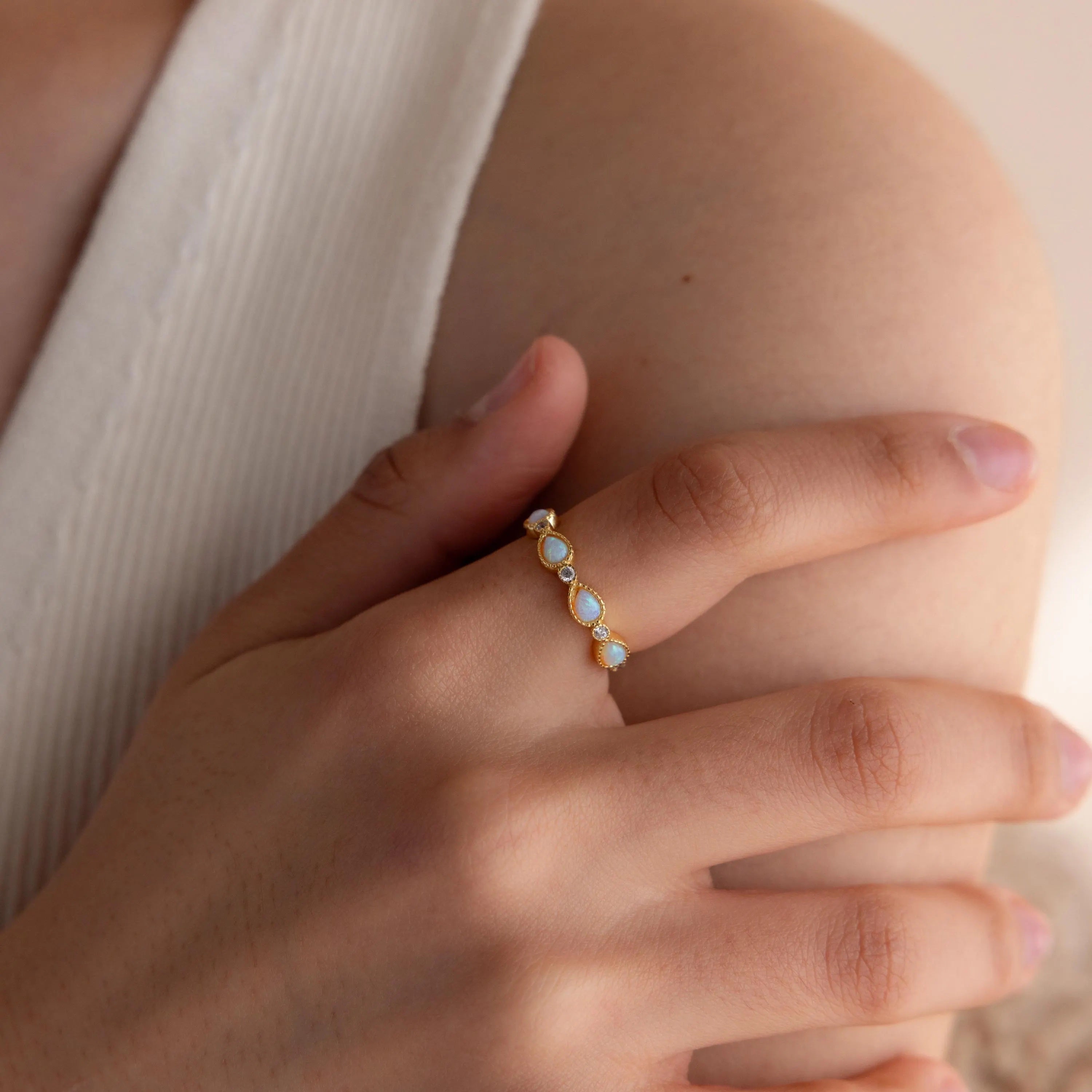 A hand wearing the Opal Diamond Teardrop Ring gently rests on a bare upper arm, showcasing its vintage-inspired opal and diamond design.