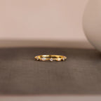 The Mixed Opal & Diamond Ring, a gold band set with opals and diamonds, is displayed on a textured gray surface against a softly blurred background.