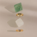 Two Baguette Signet Rings with rectangular gemstones are displayed beside green and white crystals on a neutral background, making a modern statement.