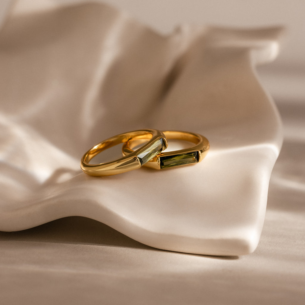 Two Peridot Baguette Signet Rings with rectangular stones rest on a white, wavy ceramic dish, each piece a modern statement ring highlighting the distinctive elegance of the Peridot Baguette Signet Ring design.