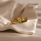 Two Peridot Baguette Signet Rings with rectangular stones rest on a white, wavy ceramic dish, each piece a modern statement ring highlighting the distinctive elegance of the Peridot Baguette Signet Ring design.