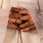 Close-up of hands with gold rings, including a modern statement ring and the Peridot Baguette Signet Ring, styled with a cream textured long-sleeve garment.