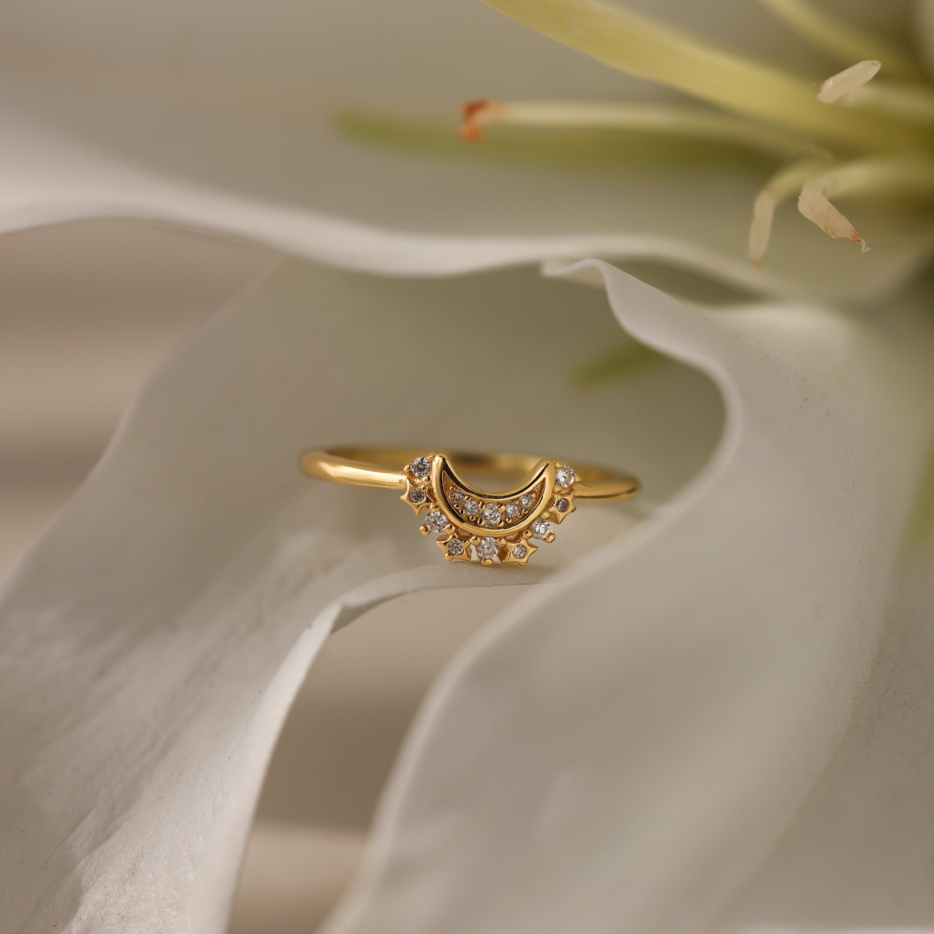 The Diamond Crescent Moon Ring, featuring sparkling diamonds and a gold crescent moon, is elegantly displayed atop a white flower petal, highlighting its celestial charm.