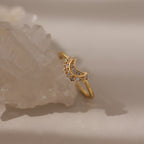 The Diamond Crescent Moon Ring, featuring a gold band with a crescent moon and small diamonds, is displayed on a clear crystal against a neutral background.