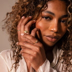 Woman with curly hair wearing a cream blouse poses with her hand near her face, showcasing the Diamond Crescent Moon Ring and gold rings.