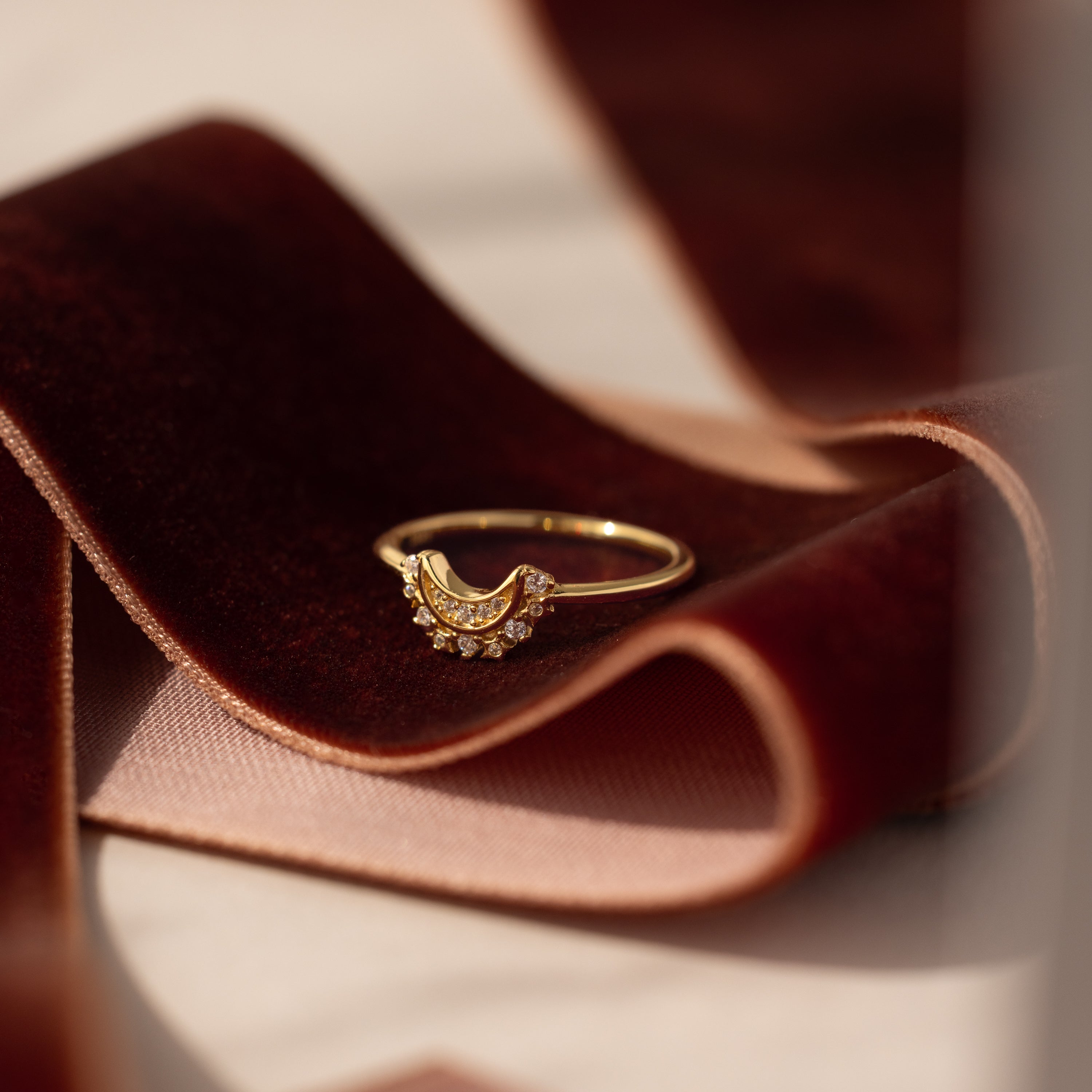 The Diamond Crescent Moon Ring is displayed on a folded piece of dark red velvet fabric.