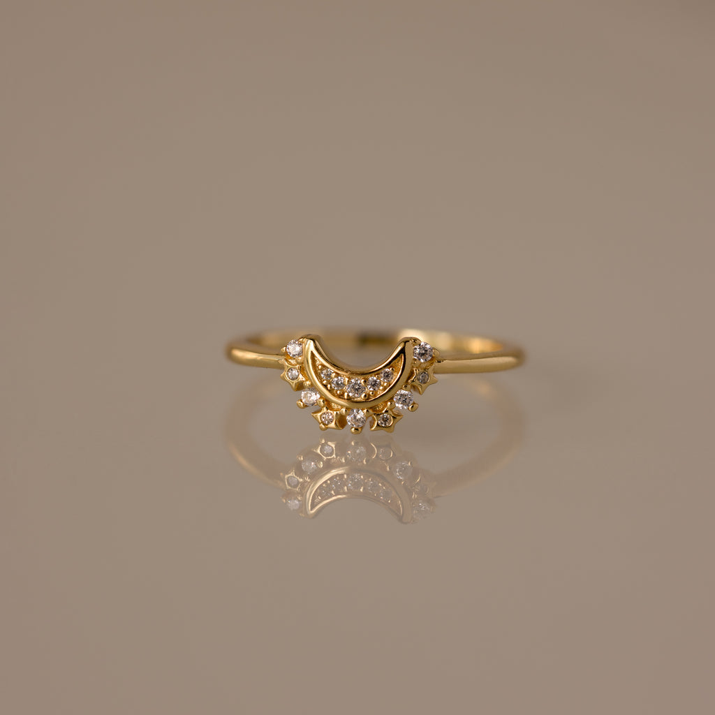 The Diamond Crescent Moon Ring features small sparkling stones and is displayed on a reflective surface—a celestial accessory perfect for adding shimmer to any look.