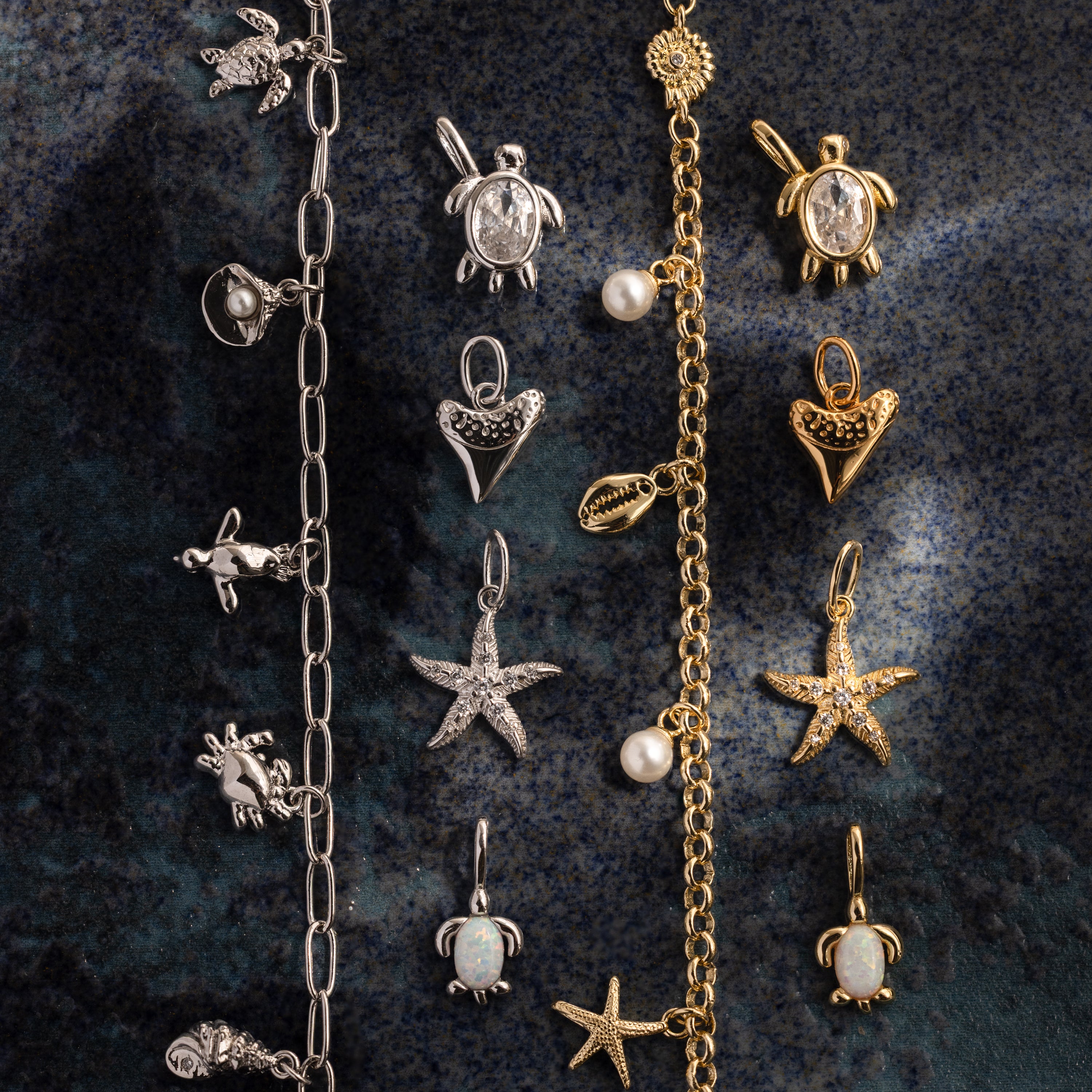 The Dainty Shark Tooth Charm in 18K Gold shines among ocean-themed bracelets and charms—turtles, hearts, starfish, and pearls—perfect coastal jewelry displayed on a dark surface.