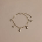 Seaside Charm Bracelet in Silver: Features five ocean-inspired charms—heart, angel, and animal—on a silver chain, displayed against a neutral beige background.