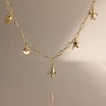 Seaside Charm Necklace in 18K Gold: Delicate gold chain with small seaside charms, ideal as beach or summer jewelry, shown on a neutral beige background.