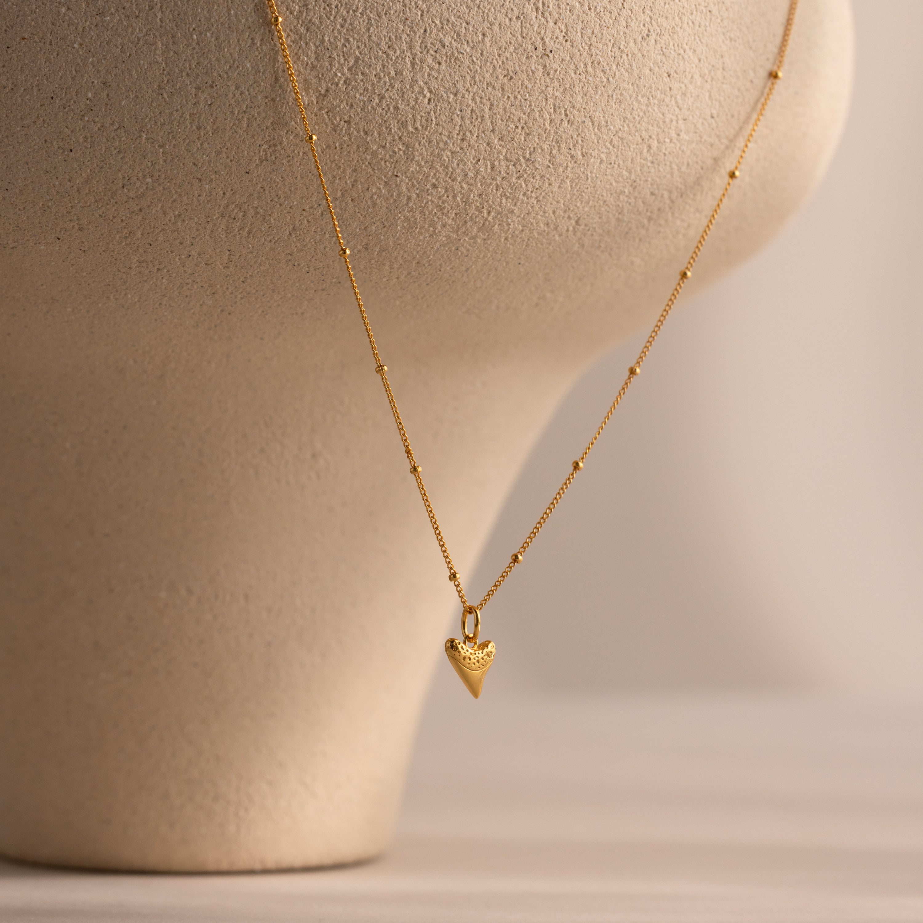 The Shark Tooth Necklace in 18K Gold, ideal for coastal jewelry lovers, is displayed on a textured beige mannequin bust against a neutral background.