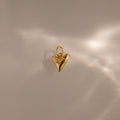 The Dainty Shark Tooth Charm in 18K Gold pairs with a textured gold heart pendant, capturing coastal elegance on a softly lit, smooth surface.