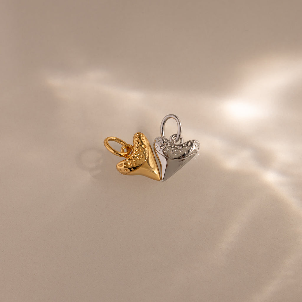 The Dainty Shark Tooth Charm in Silver captures coastal jewelry vibes, featuring textured details and displayed on a neutral background with soft, elegant light reflections.