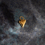 The Dainty Shark Tooth Charm in 18K Gold rests on a blue marbled surface, making it an ideal accessory for coastal jewelry enthusiasts.