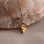 An 18K gold shark tooth necklace, ideal for lovers of coastal jewelry, is displayed on an iridescent seashell background.