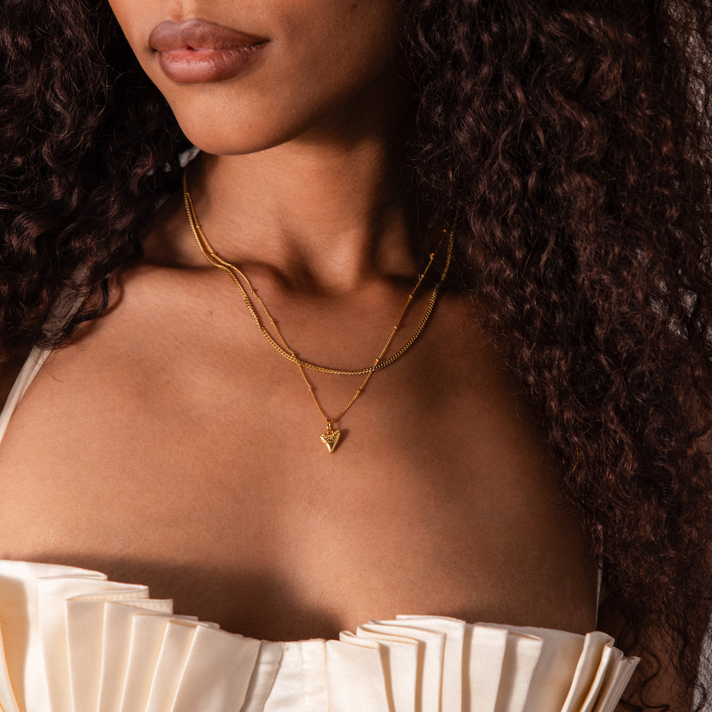 Woman wears a cream pleated top and the Shark Tooth Necklace with layered gold chains, channeling a chic beachside aesthetic.