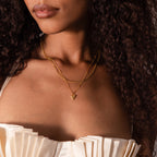Woman wears a cream pleated top and the Shark Tooth Necklace with layered gold chains, channeling a chic beachside aesthetic.